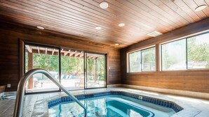 Una piscina interior con techo de madera, puertas de vidrio que dan al exterior y suelo de baldosas.