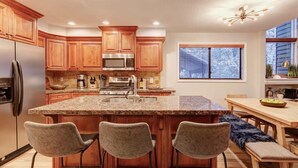 Una cocina moderna con armarios de madera, electrodomésticos de acero inoxidable y una isla de granito con taburetes.