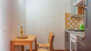 A small kitchen with a wooden table and chair, a bottle of wine, and a green dish. - Beach front apartment (Sant.Teresa di Gallura)