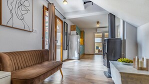 Een moderne woonkamer met een bruine bank, een witte koelkast, een zwarte houtkachel, en een eethoek met een houten tafel en een schaal druiven.