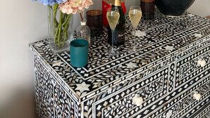 Ett dekorativt konsolbord med en spegel, en flaska champagne, två glas och en vas med blommor.