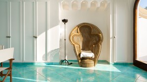 A room with a teal tiled floor, a wicker chair with a white cushion, a standing floor lamp, and white doors with decorative moldings.