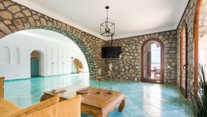 A spacious room with a stone wall, a wooden table, and a television mounted on the wall. - La Torre del Vervece (Massa Lubrense)