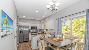 A modern kitchen with white cabinets, stainless steel appliances, and a dining area with a wooden table and chairs. - Discount! Walk to Beach, Golf,  Pool, Arcade, Beautiful and peaceful community (North Myrtle Beach)