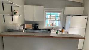 Una cocina con armarios blancos, microondas, cafetera y refrigerador. Hay tres taburetes negros en la barra.