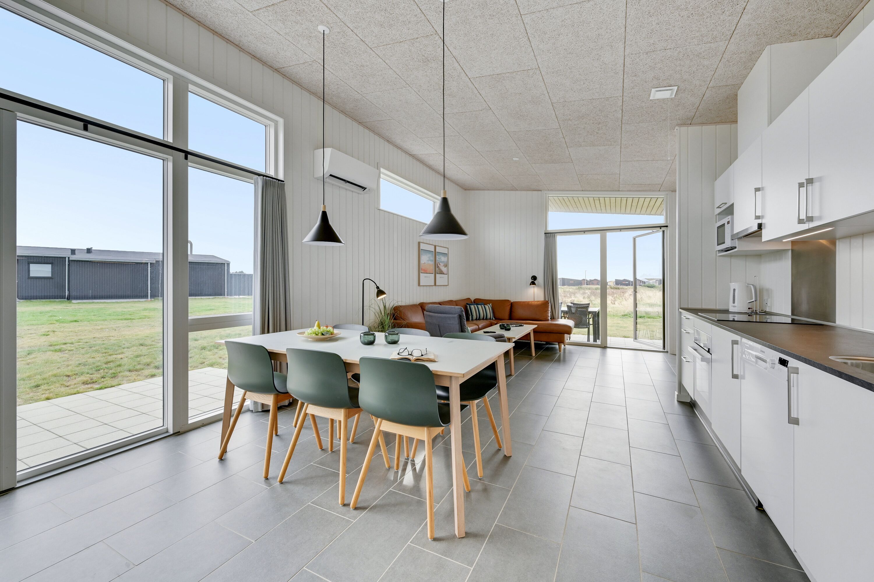 A modern kitchen with white cabinets, a dining area with a table and chairs, and large windows offering a view of the outdoors.