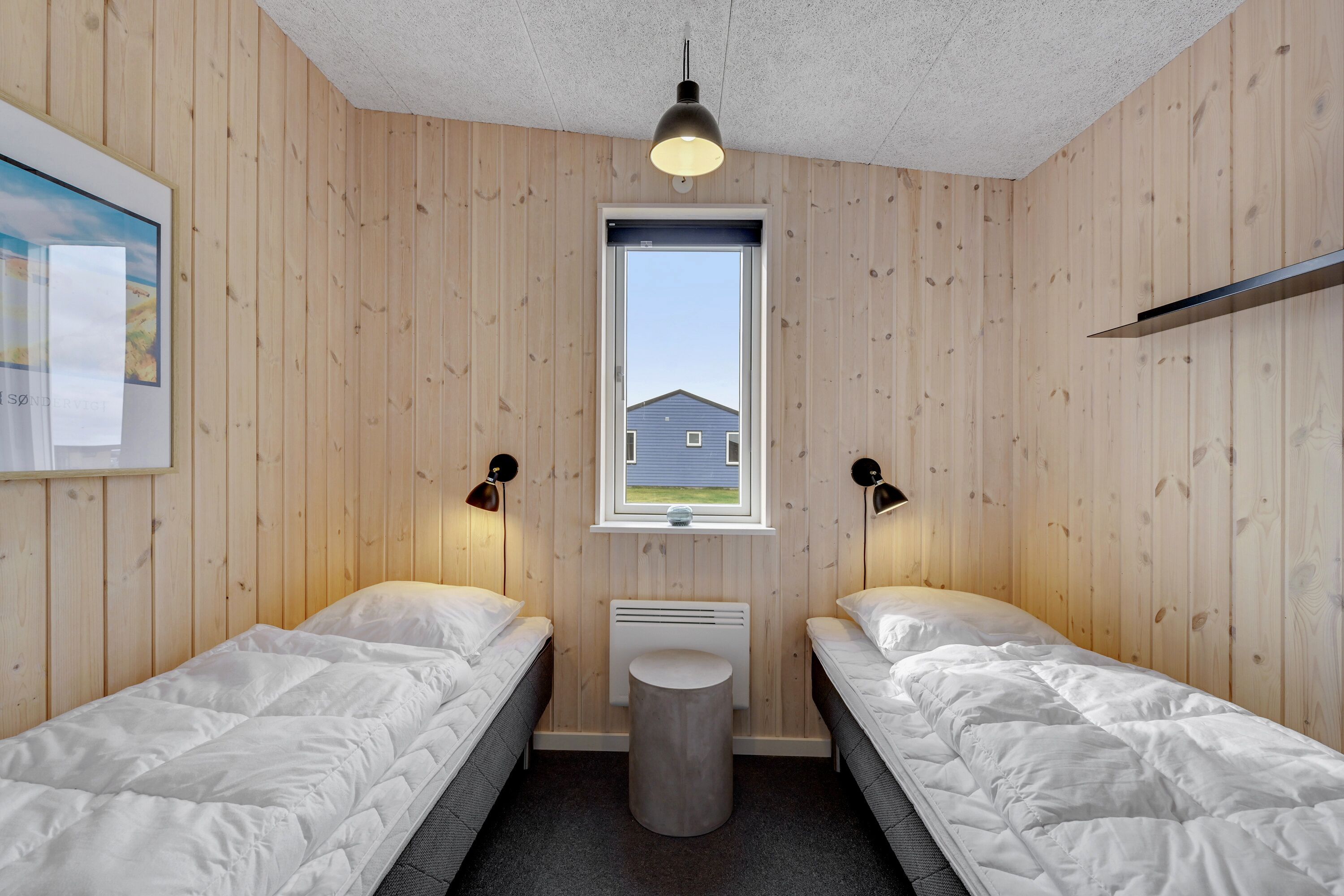 A room with two beds, a window, a radiator, and a small stool.
