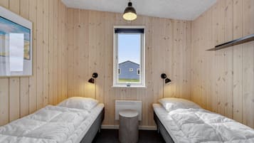 A room with two beds, a window, a radiator, and a small stool.