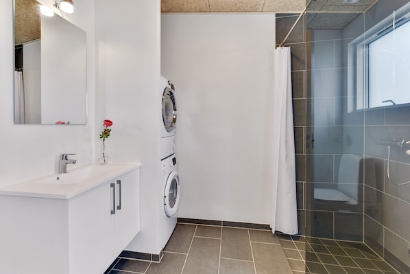 A modern bathroom with a built-in washing machine, a sink, and a shower area.