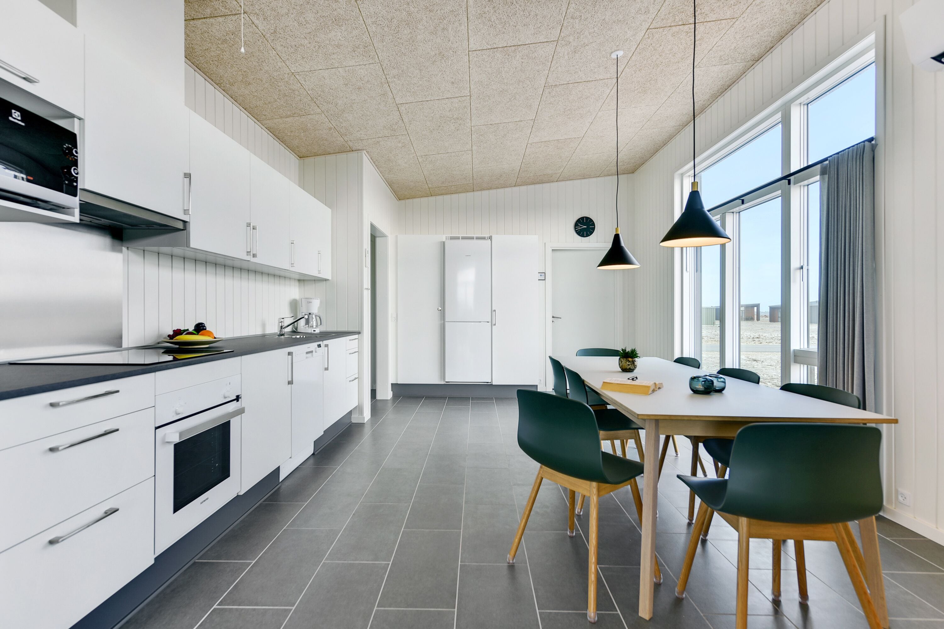 Una cucina moderna con mobili bianchi, un piano di lavoro nero e un'area pranzo con tavolo in legno e sedie verdi.