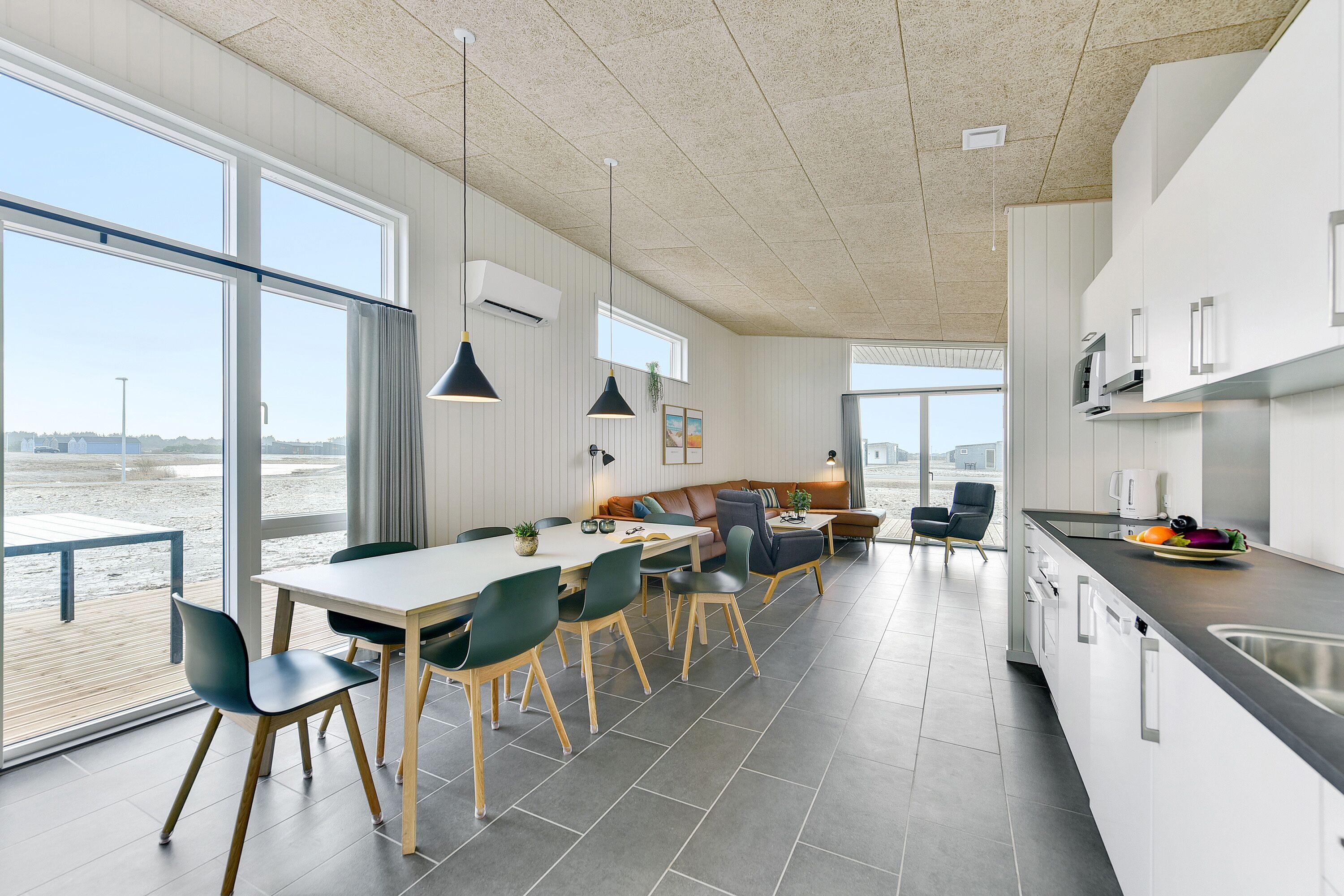 A modern kitchen with a large island, a dining area with a view, and a spacious living area with a large window overlooking a beach.