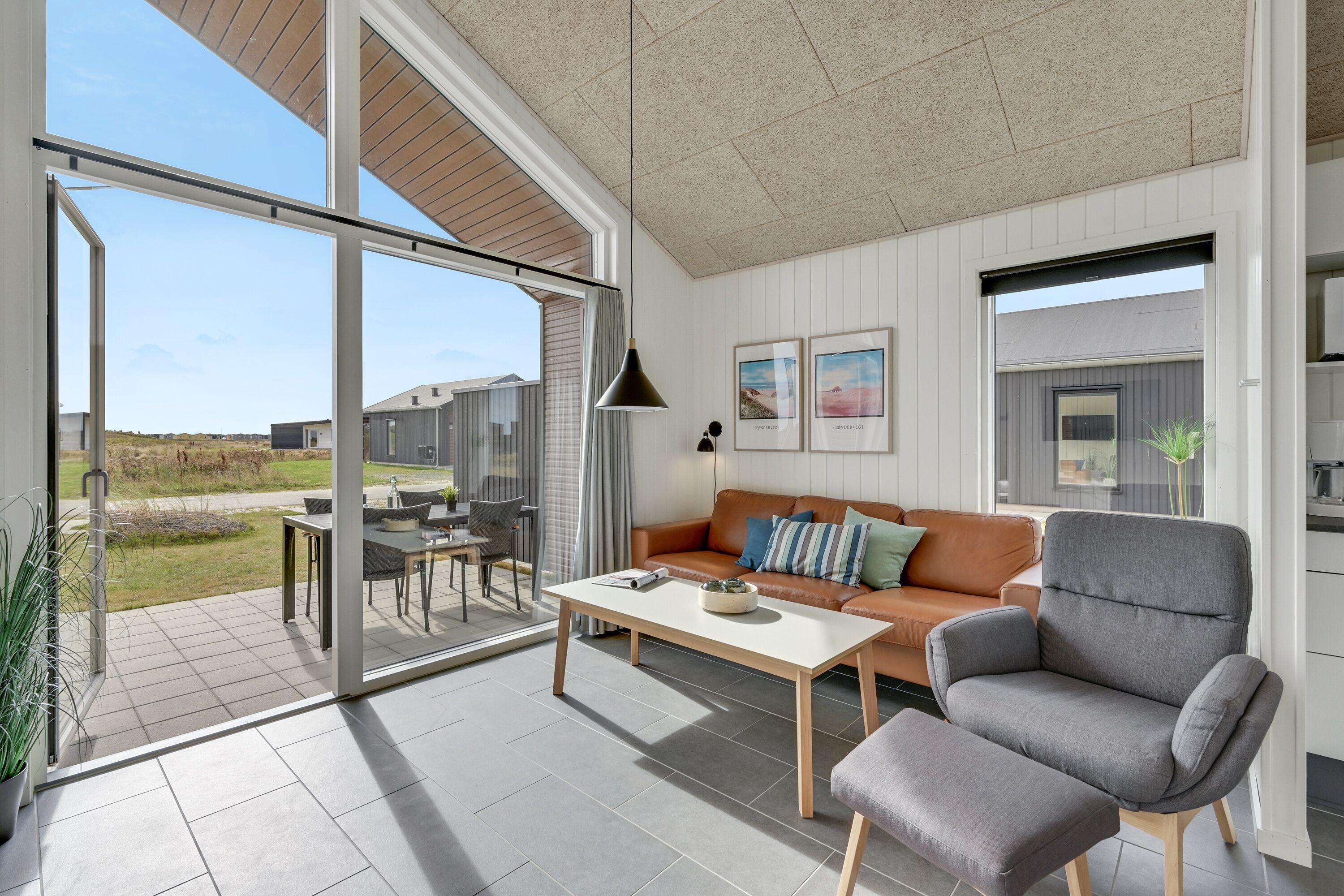 Una sala de estar moderna con un sofá, un sillón y una mesa de centro, y grandes puertas correderas de vidrio que dan a un patio exterior.