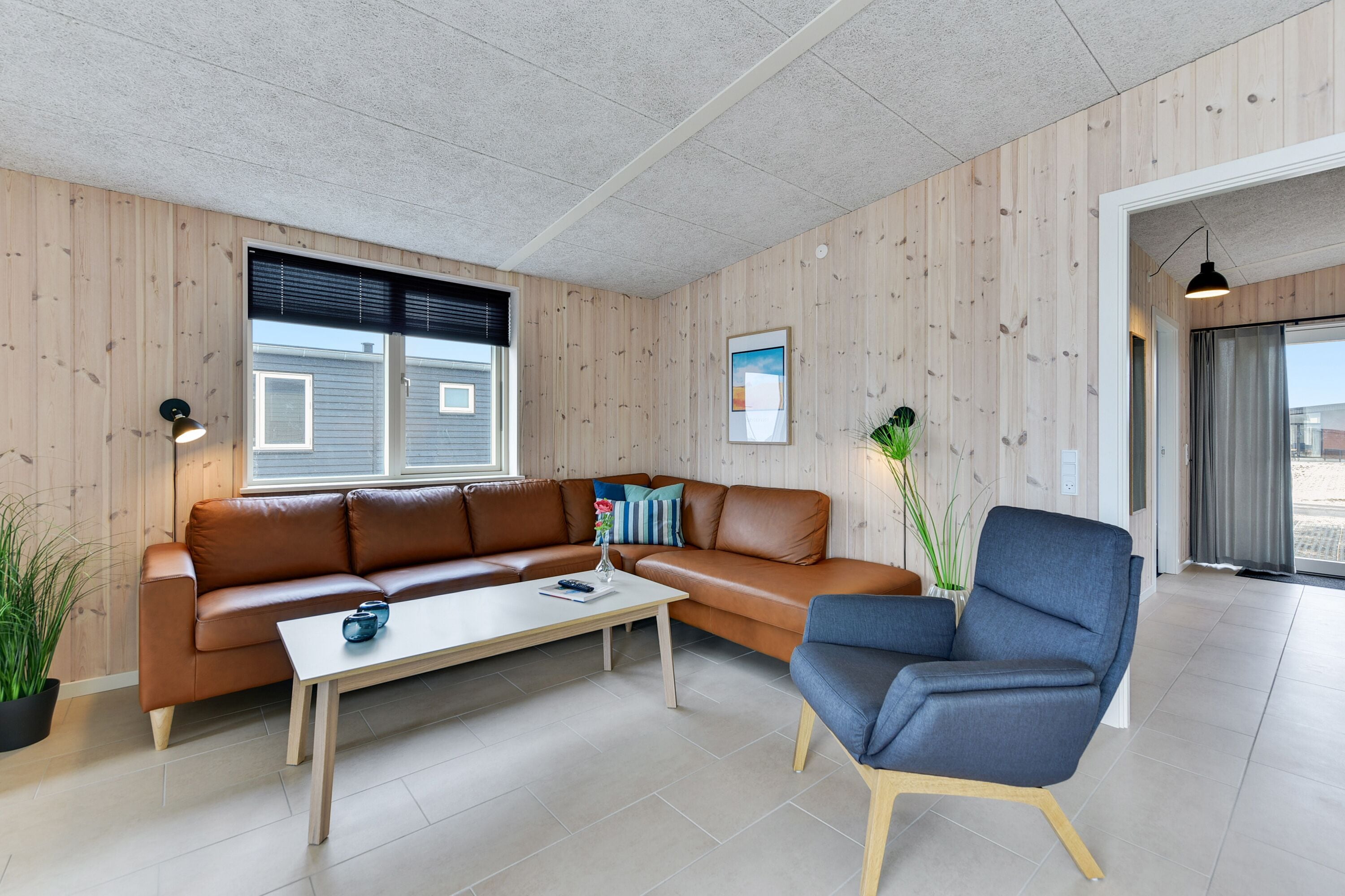 Una sala moderna con un sofá de cuero marrón, una mesa de centro blanca y un sillón azul.