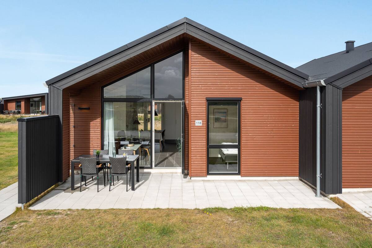 Un edificio moderno con una amplia entrada de vidrio, un patio con mobiliario exterior y una señal con el número del lugar.