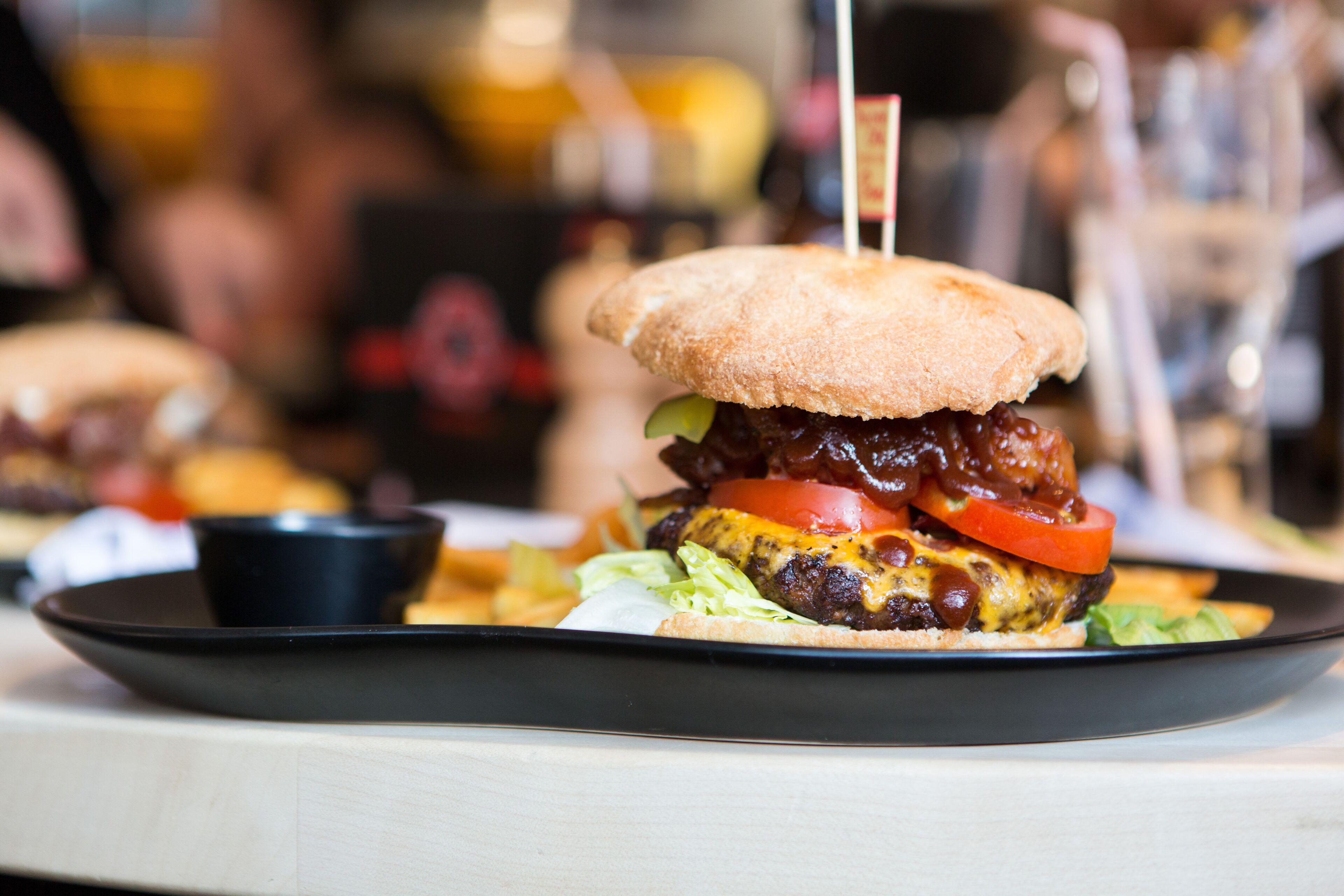 Un hamburger servi sur une assiette noire, composé d’un pain aux graines de sésame, de laitue, de tomate et d’un steak haché.