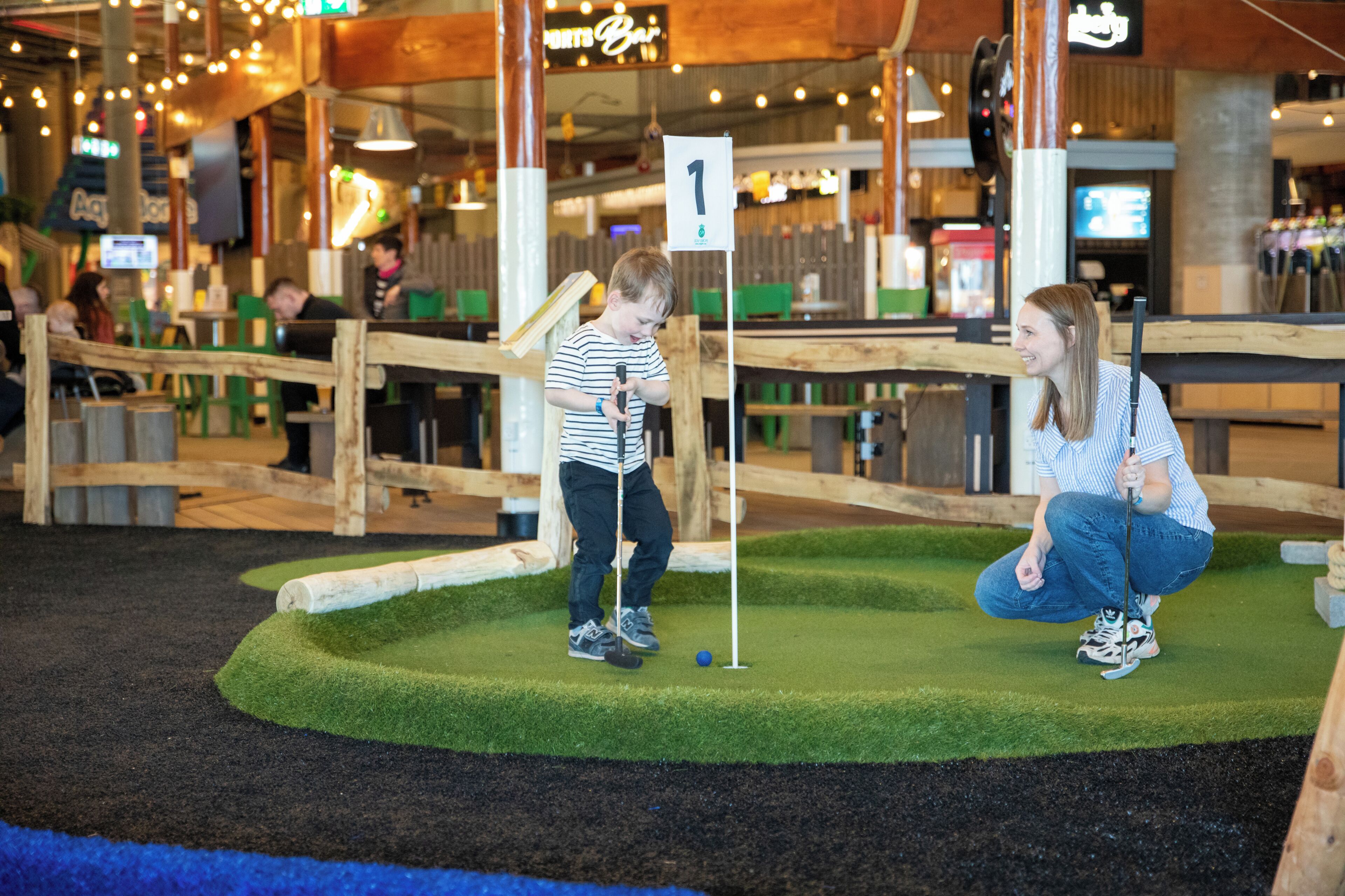 Ein Minigolfplatz mit Holzzaun, einer grünen Spielfläche und einer Fahne mit der Nummer 1.