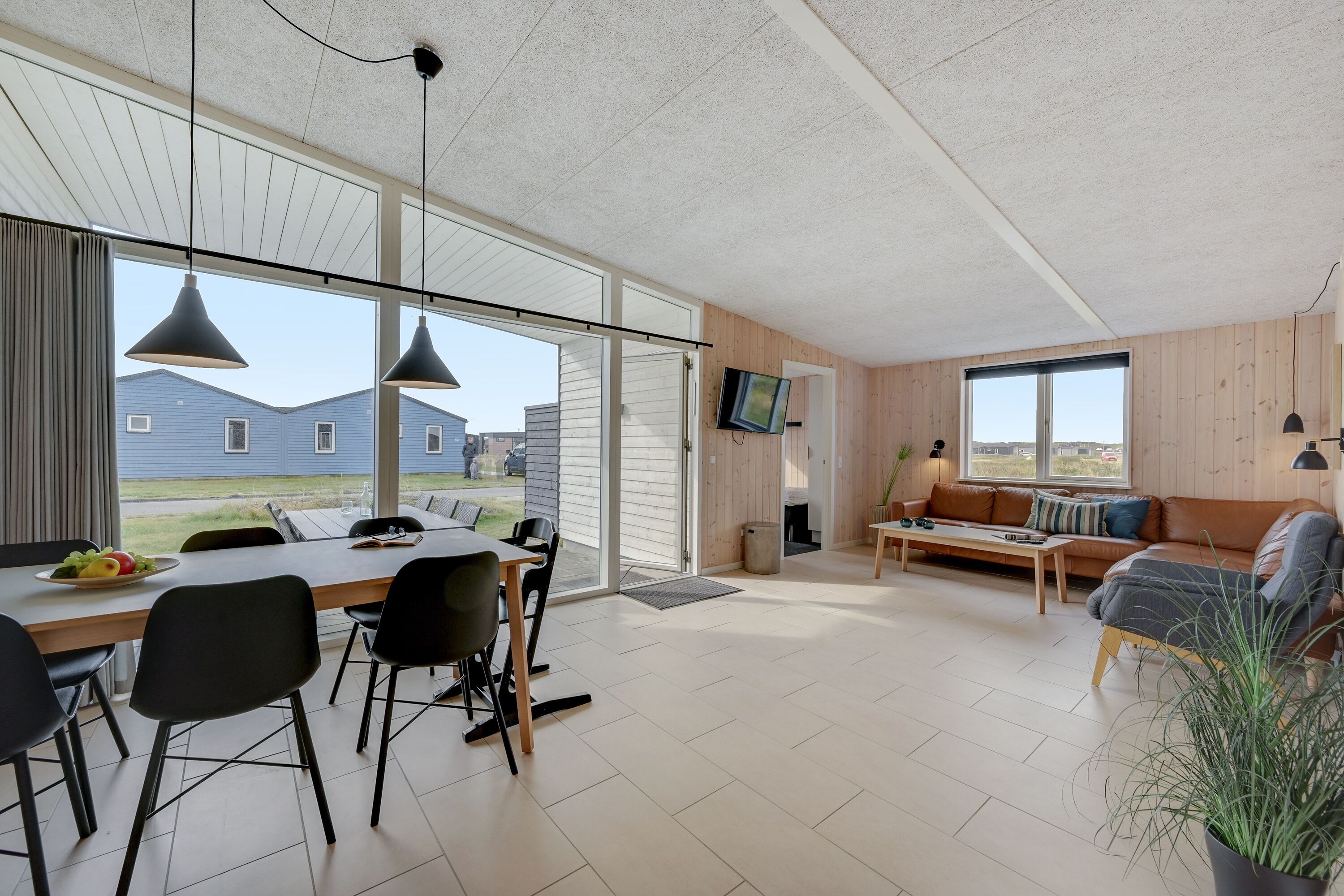 A spacious living area with a dining table, chairs, a sofa, and a TV mounted on the wall.