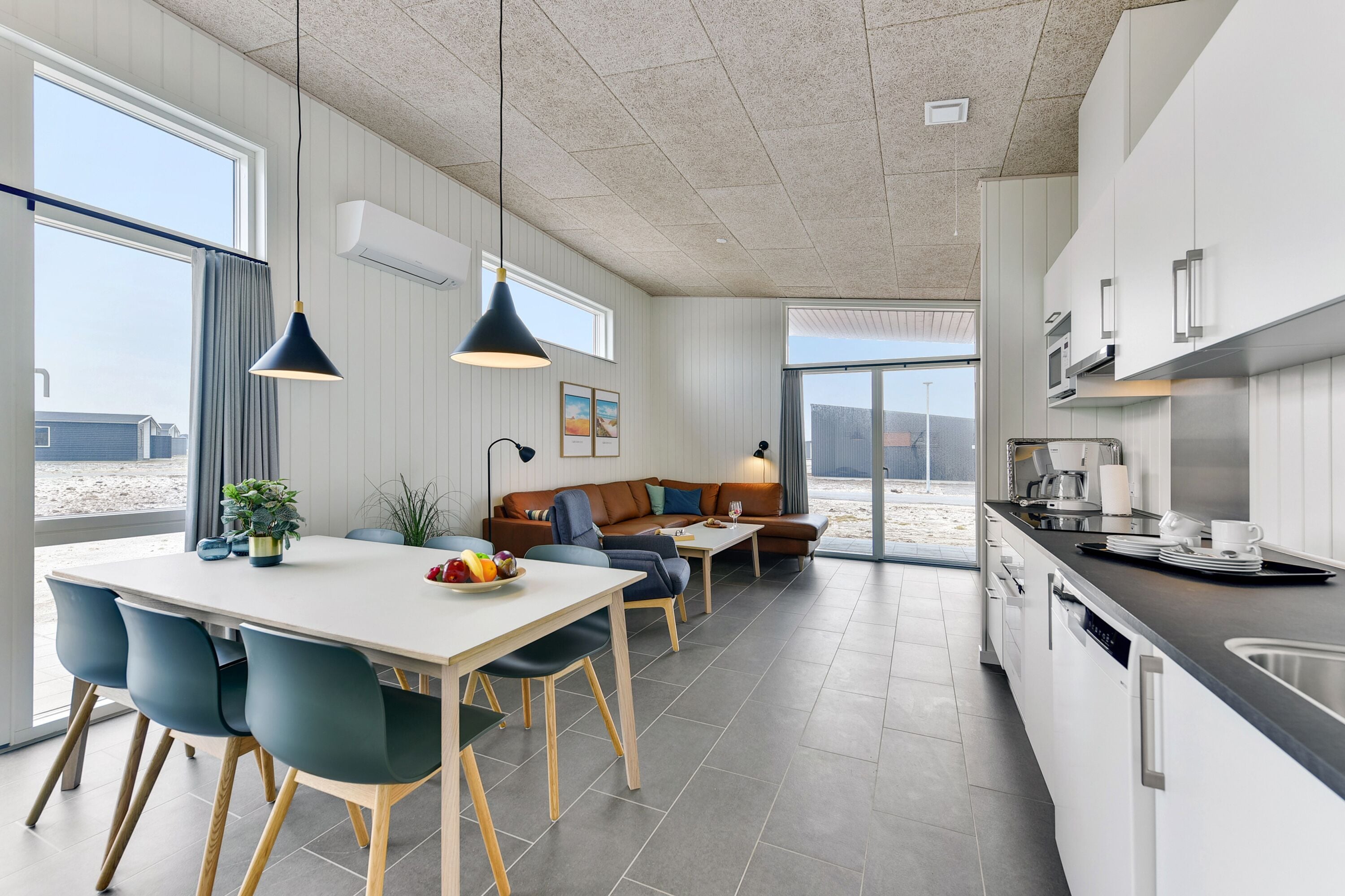 Una cocina moderna con armarios blancos, un lavamanos de acero inoxidable y una zona de comedor con una mesa blanca y sillas azules.
