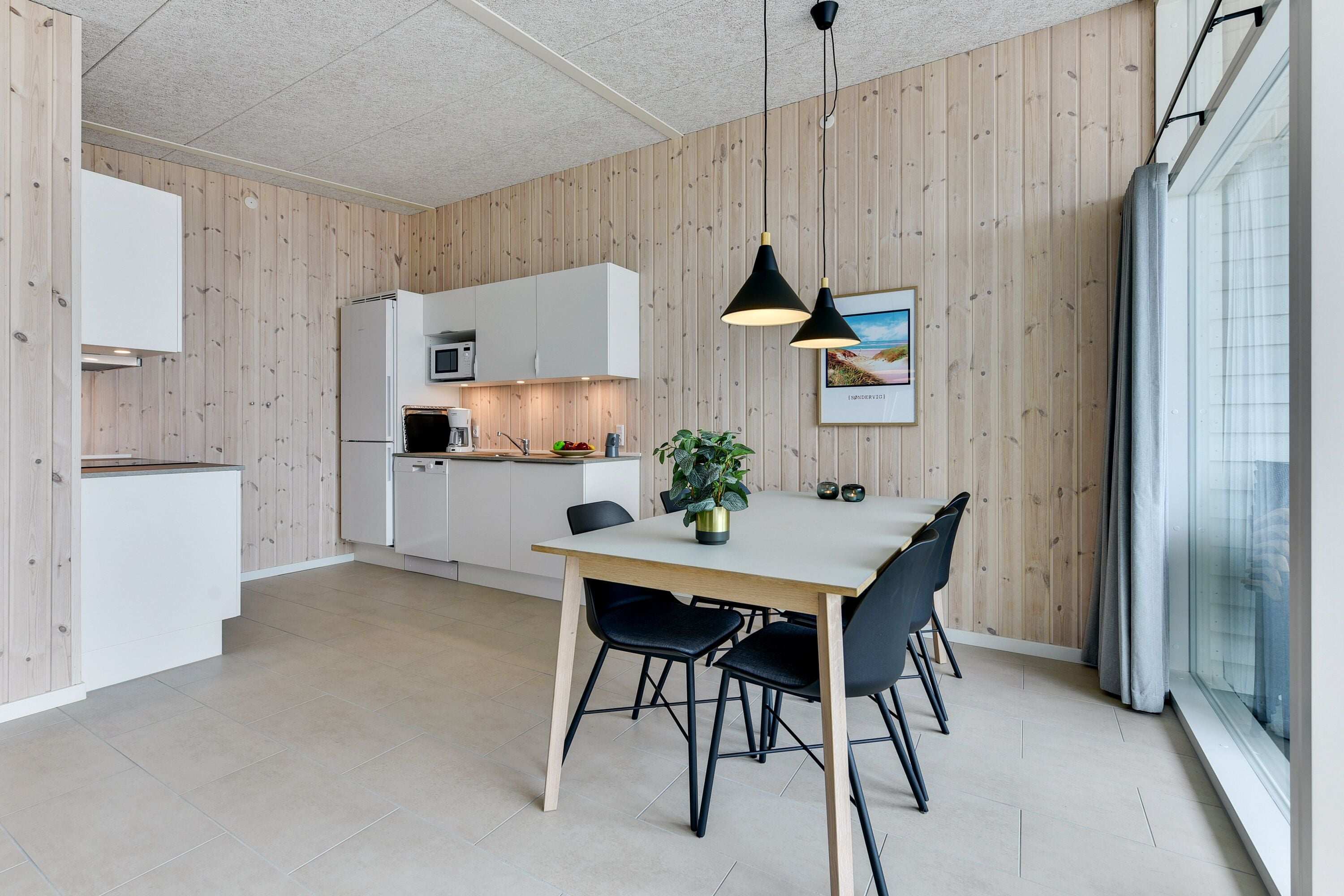 Moderni keittiö, jossa on puupanelointi, ruokailutila pöytineen ja tuoleineen sekä suuri ikkuna, josta on kaunis näköala.