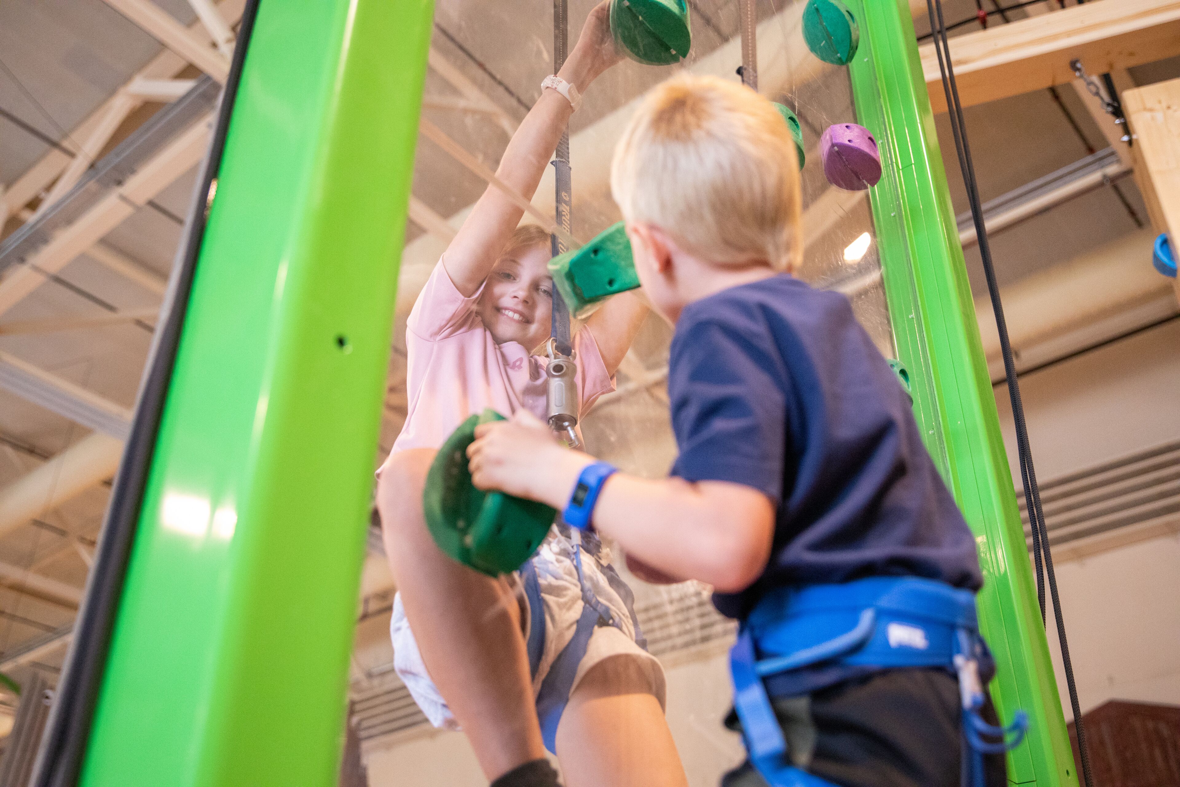 A person climbing a green climbing wall with safety gear.