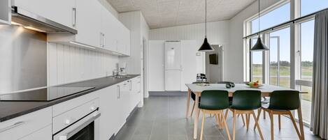Una cocina moderna con armarios blancos, encimera negra y un comedor con mesa y sillas.