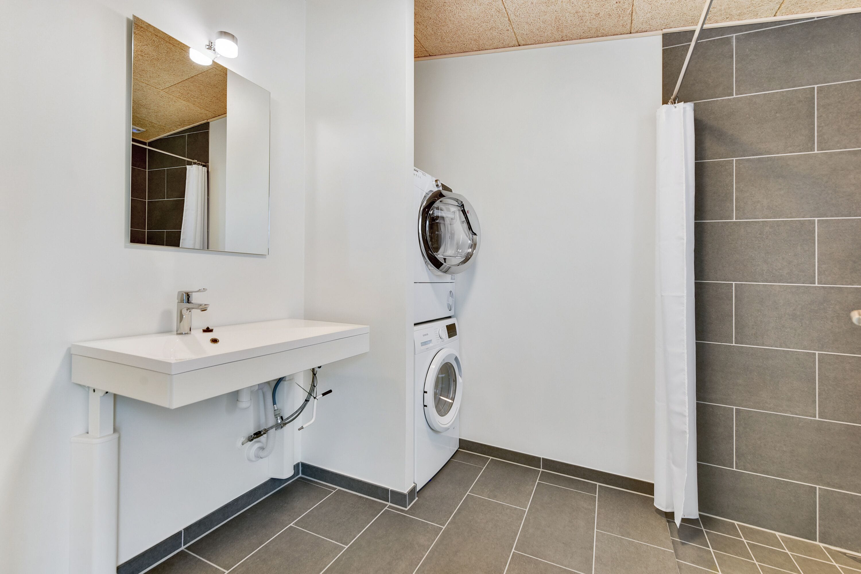 Een moderne badkamer met een witte wastafel, een spiegel, een wasmachine en een douche.