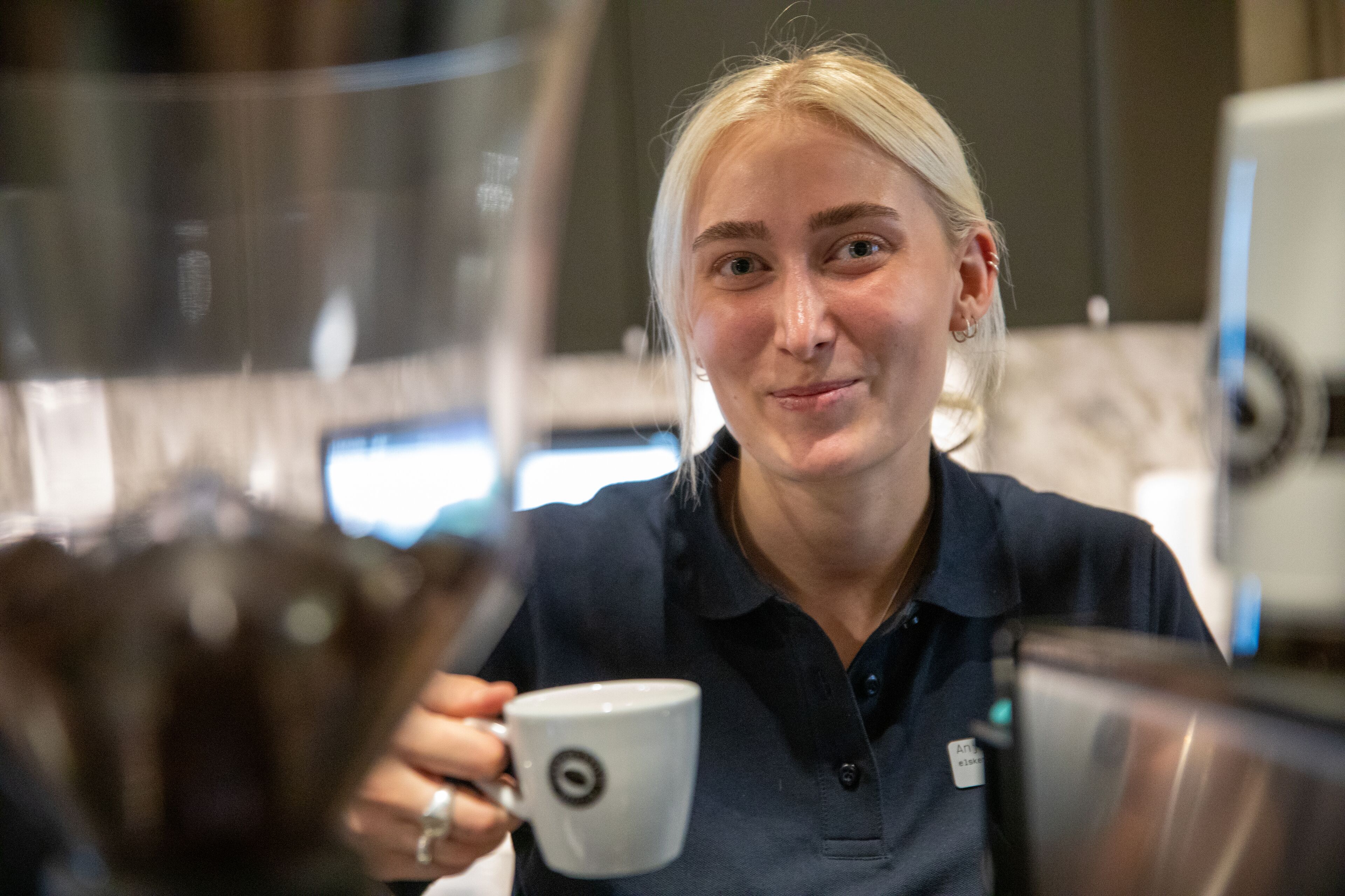 Una persona sosteniendo una taza en una cocina moderna con electrodomésticos de acero inoxidable.