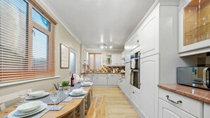 Una cocina moderna con armarios blancos, una mesa de comedor de madera dispuesta con platos y vasos, y un horno empotrado.