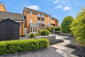 A residential building with a brick facade, a garage, and a well-maintained garden with hedges and a stone wall.