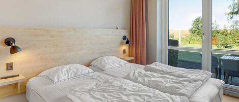 A hotel room with a large bed, two bedside lamps, a wooden headboard, and a view of the outdoors through a large window.