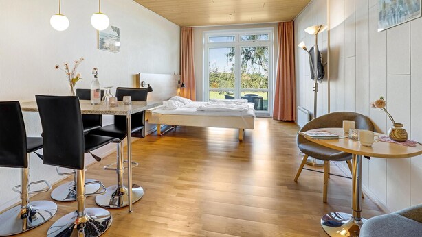 Ein modernes Hotelzimmer mit Holzboden, einem Bett, einem Esstisch mit Stühlen und einem großen Fenster mit Vorhängen.