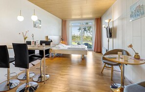 Een moderne hotelkamer met een houten vloer, een bed, een eettafel met stoelen en een groot raam met gordijnen.