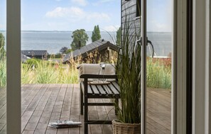 A wooden deck with a bench and a wicker basket, overlooking a body of water and a distant building. - Stunning home in Sjølund with sauna (Sjølund)