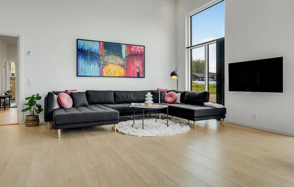 A modern living room with a sectional sofa, a round coffee table, and a large abstract painting on the wall. - Stunning home in Sjølund with sauna (Sjølund)