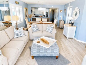 A living room with a sofa, ottoman, and a dining area with a kitchen in the background.