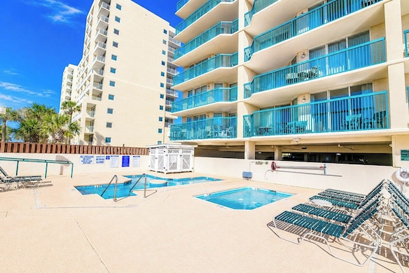 A hotel pool area with multiple swimming pools, sun loungers, and a building with balconies.