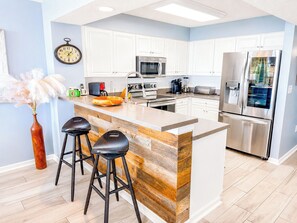 Cozinha moderna com armários brancos, geladeira de aço inoxidável, micro-ondas e ilha de madeira com banquetas.