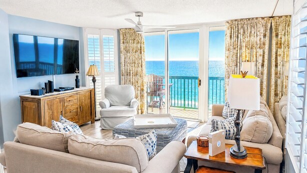 Una sala de estar con sofá, sillón, mesa de centro, televisor y un balcón con vista al mar.