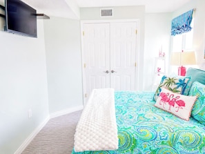 A bedroom with a bed, a bench, a TV mounted on the wall, and a white door.
