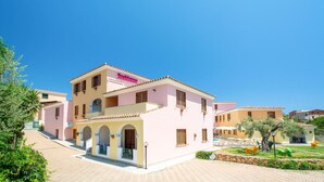 Un edifici rosa amb un rètol que diu "Residence" i una zona de piscina al fons.