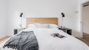 Una cama bien hecha con un cabecero de madera, dos mesitas de noche con lámparas y una revista sobre la cama.
