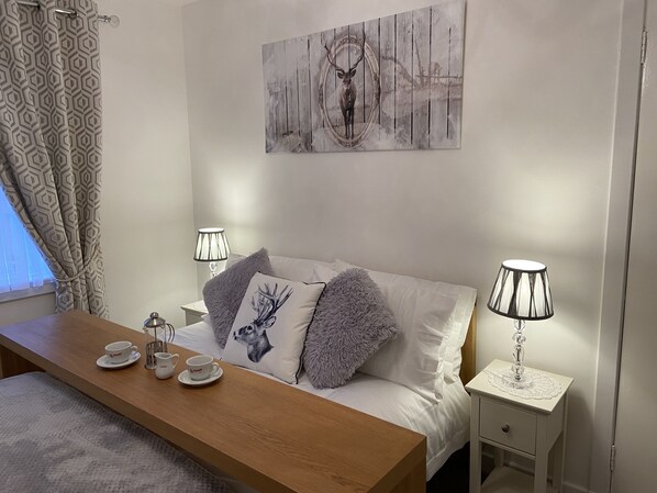A neatly arranged bedroom with a bed, bedside tables, lamps, and a painting on the wall.