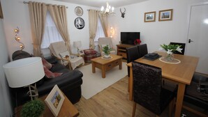 A living room with a sofa, coffee table, and TV. There is a dining table with chairs. The room has curtains, a chandelier, and wall decorations. - Historic Old Town 2 Bed Ground Floor Apartment (Stirling)