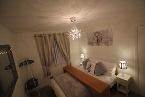 Un dormitorio con cama, lámparas de noche, lámpara colgante, un espejo y una obra de arte en la pared.