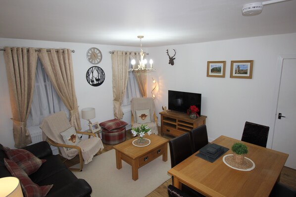 Una sala de estar con sofá, sillón, mesa de centro de madera y mueble para televisión.