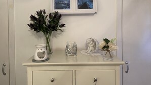 A bathroom vanity with a white cabinet, a vase with dark foliage, a white ceramic pitcher, a glass sculpture, and a framed photograph above the mirror. - Historic Old Town 2 Bed Ground Floor Apartment (Stirling)