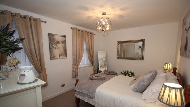 A bedroom with a bed, bedside lamps, a dresser, a mirror, and a chandelier. - Historic Old Town 2 Bed Ground Floor Apartment (Stirling)