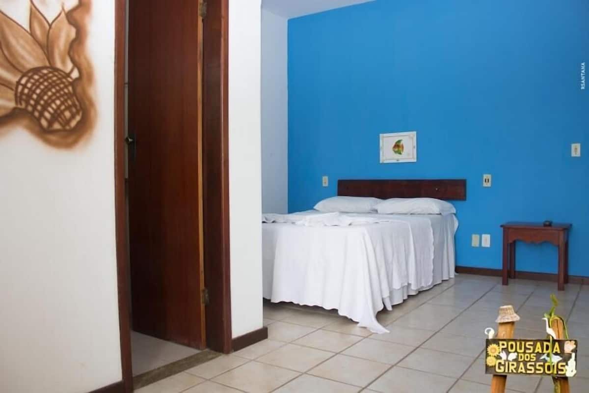 A room with a bed, a wooden headboard, a small table, and a wall with a pineapple picture.