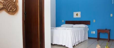 Una habitación con una cama, cabecera de madera, una mesita pequeña y un cuadro de piña en la pared.