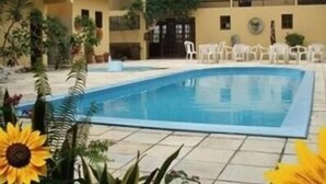 Un área de piscina con una pileta rectangular, rodeada de plantas en macetas y sillas blancas.